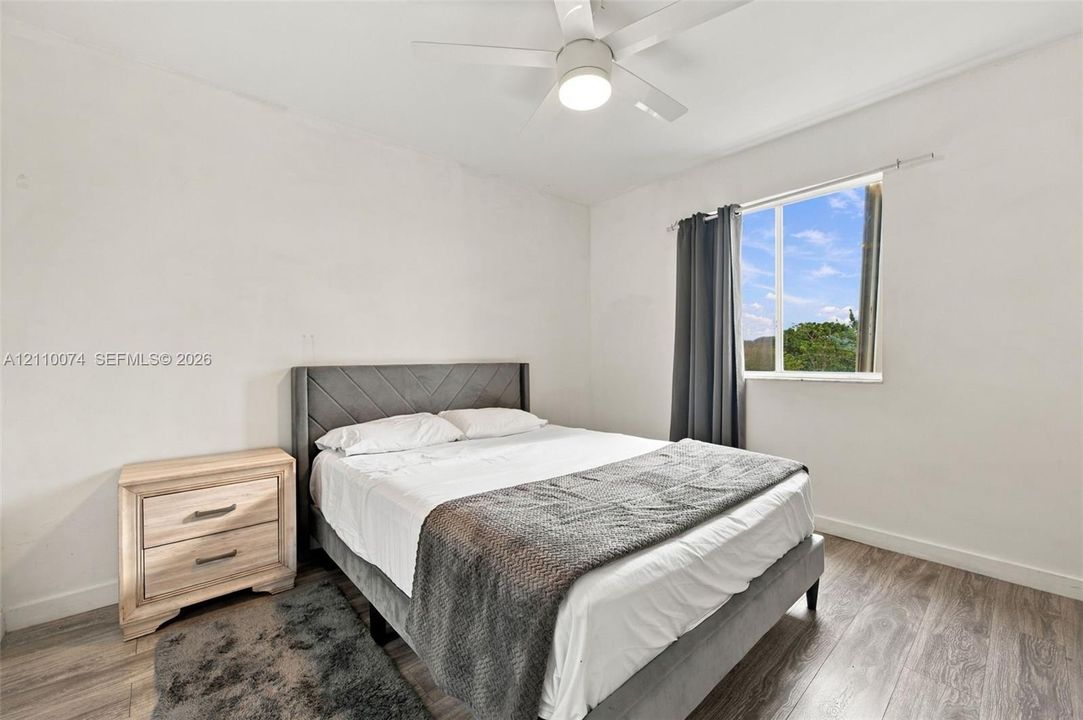 Neutral-toned room featuring wood-finish flooring, a white ceiling fan with integrated lighting, and a single-pane window