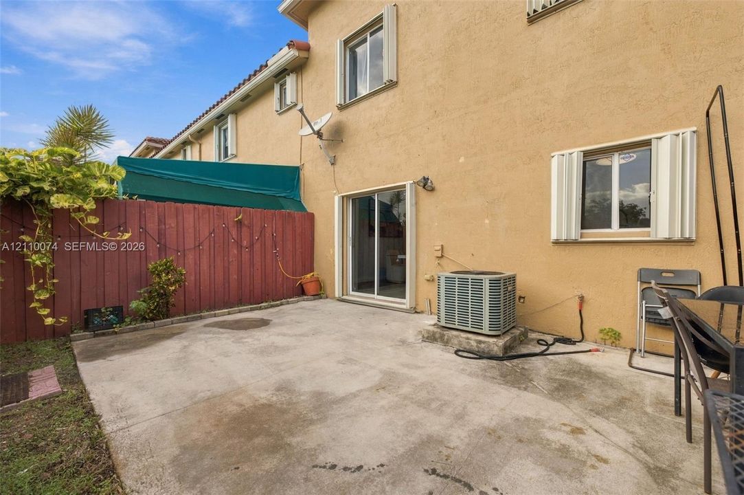 Concrete patio area enclosed by a wood privacy fence featuring sliding glass door access and exterior shutters