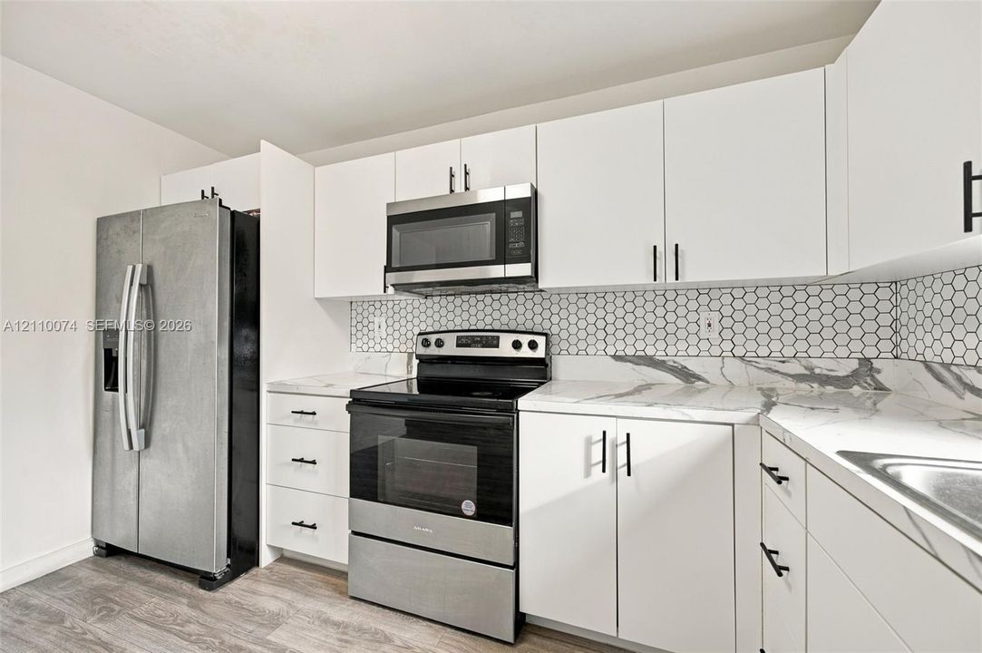 Kitchen featuring white cabinetry, stone-look countertops, hexagonal tile backsplash, stainless steel appliances, and wood-finish flooring