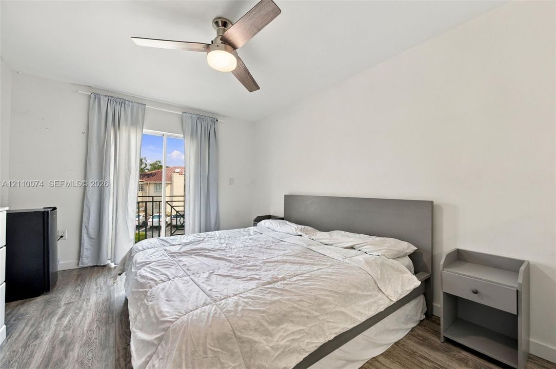 Neutral-toned room featuring wood-finish flooring, a contemporary three-blade ceiling fan with integrated lighting, and a sliding glass door providing external access to a balcony with metal railings
