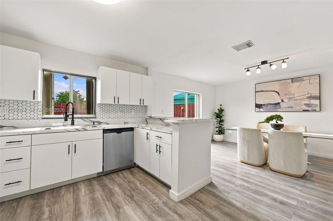 Kitchen featuring white cabinetry with matte black hardware, light-toned stone-finish countertops, geometric tile backsplash, stainless steel dishwasher, and wood-finish flooring
