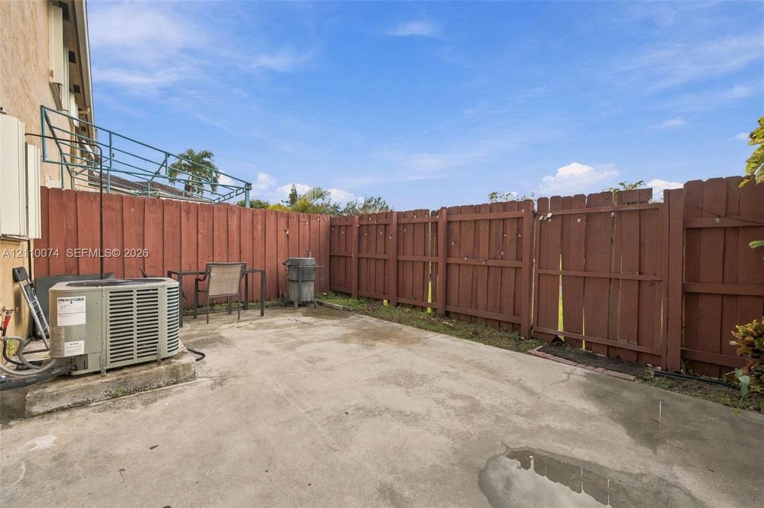 Rear concrete patio enclosed by a perimeter wood-slat fence