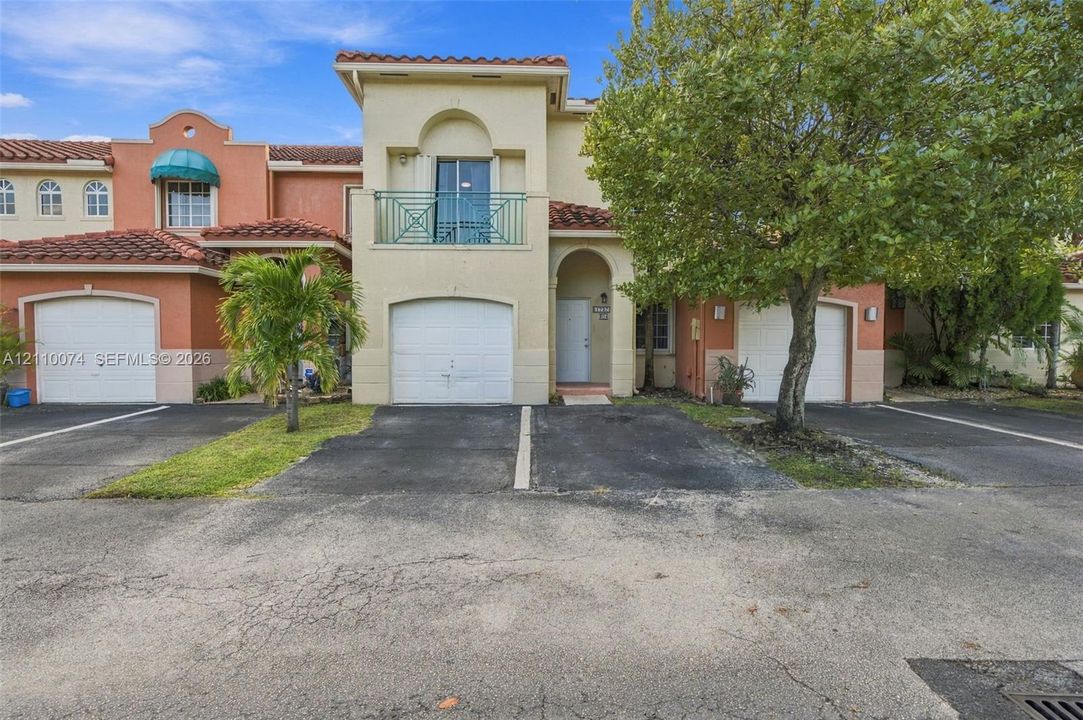 Mediterranean-inspired townhome featuring a stucco exterior, clay tile roofing, private upper-level balcony with metal railing, and attached garage