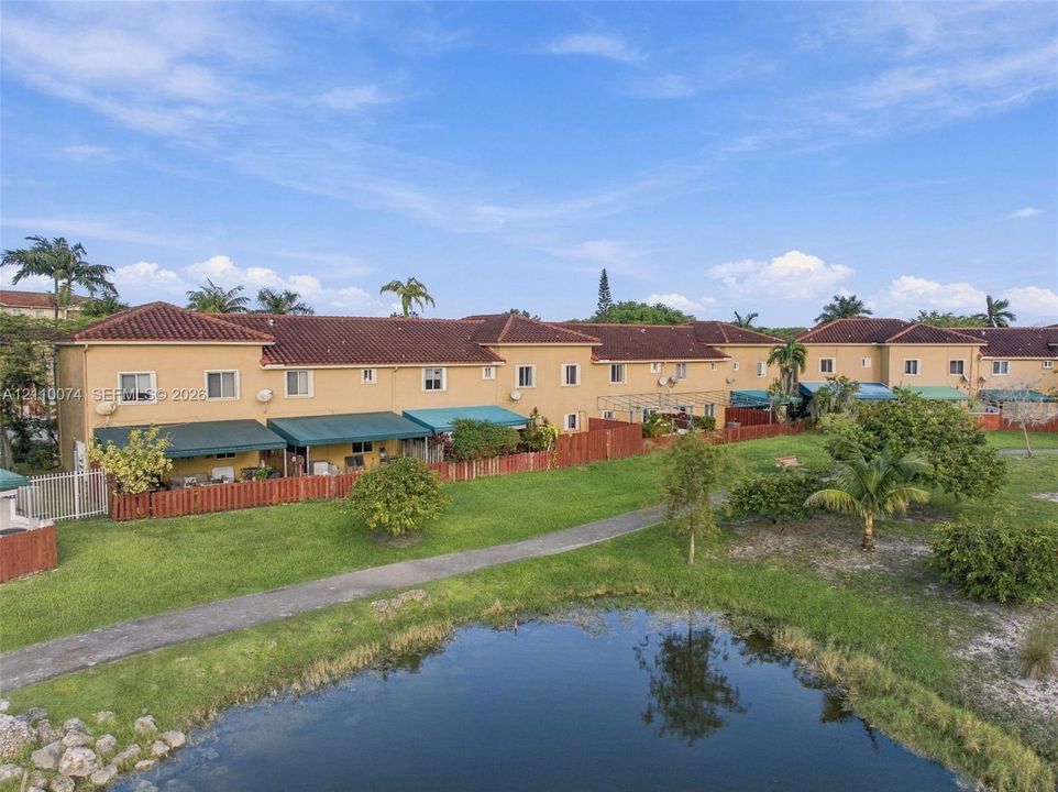 Multi-story stucco exterior featuring a tile roof, dedicated green space, paved pathways, and a water feature