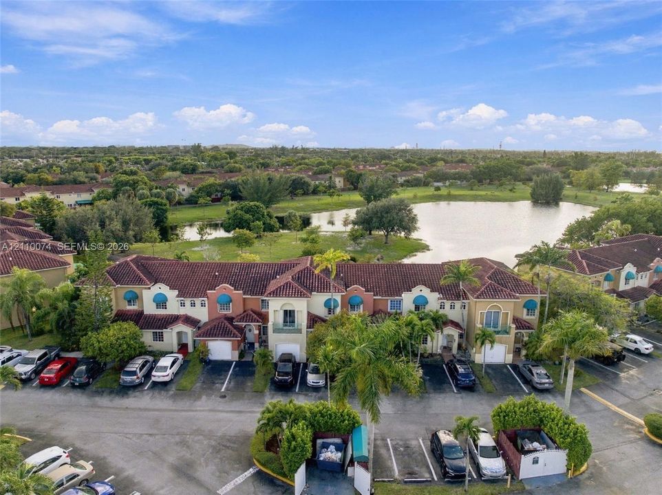 Multi-level townhome exterior featuring terracotta-style roof tiles, stucco facade, decorative blue window awnings, integrated garage bays, and mature palm landscaping