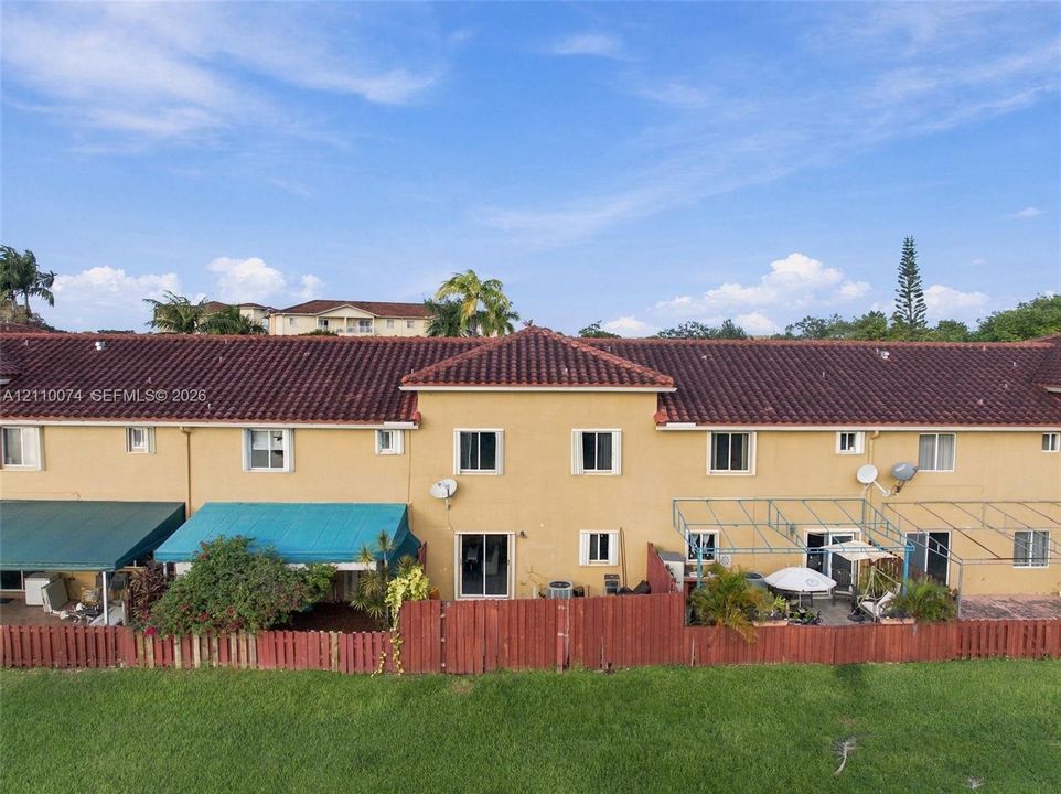 Exterior elevation featuring a stucco facade, red tile roofing, rear patio enclosures, and wood-style privacy fencing overlooking a grassy lawn