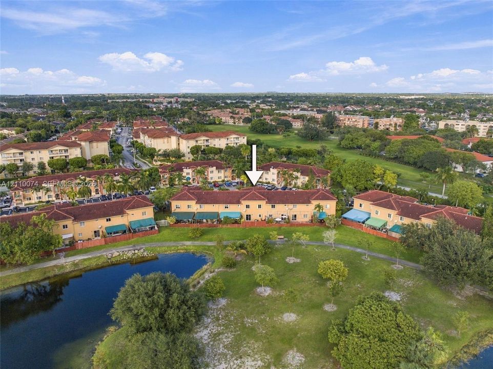 Aerial perspective of a multi-unit complex featuring terra cotta-style shingle roofing, stucco exterior, and waterfront grounds with a paved walking path