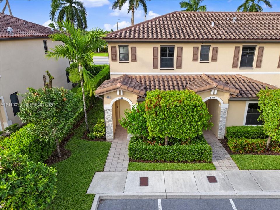 Two-story townhome exterior featuring a Spanish-tile roof, stucco siding, arched entryways with stone veneer detailing, and shuttered windows