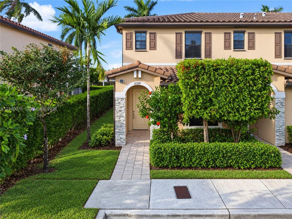 Two-story stucco exterior featuring a tile roof, arched entryway with stacked-stone facade accents, and shuttered windows