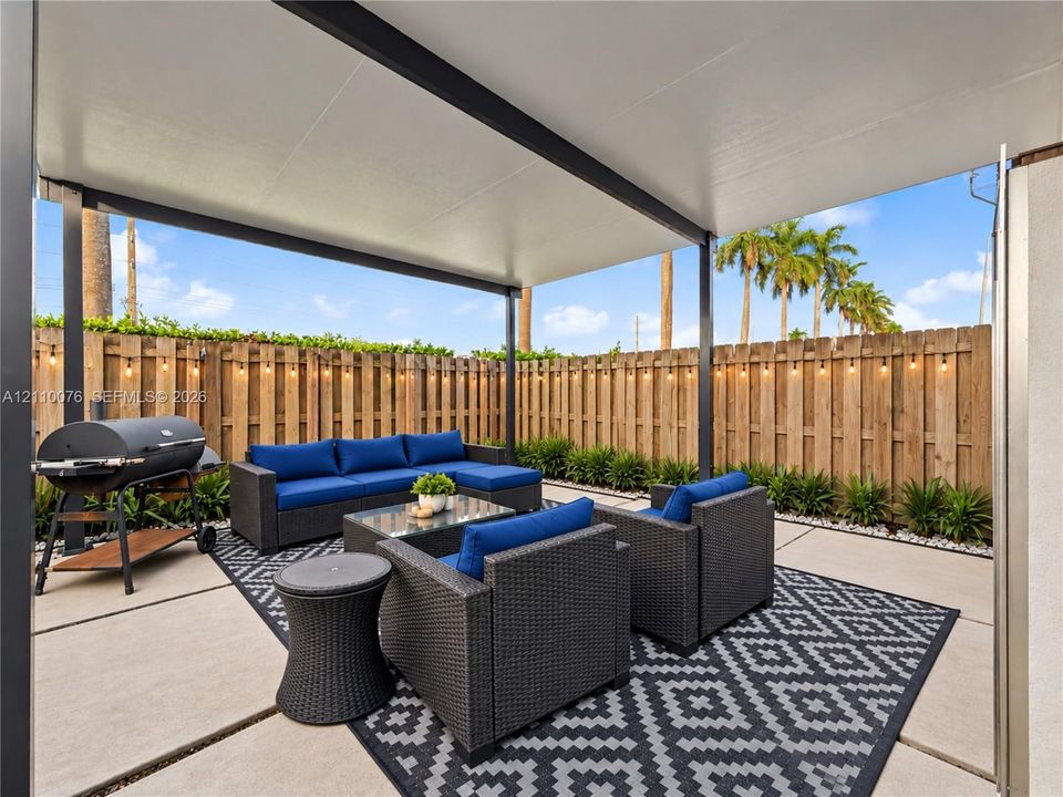 Covered concrete patio featuring a metal structural support frame, perimeter wood privacy fencing, and a white stone landscape border