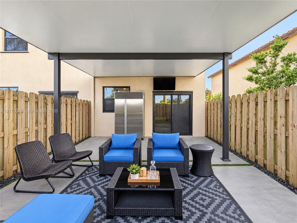 Covered concrete patio featuring a metal support structure, built-in stainless steel exterior refrigerator, and wooden privacy fencing