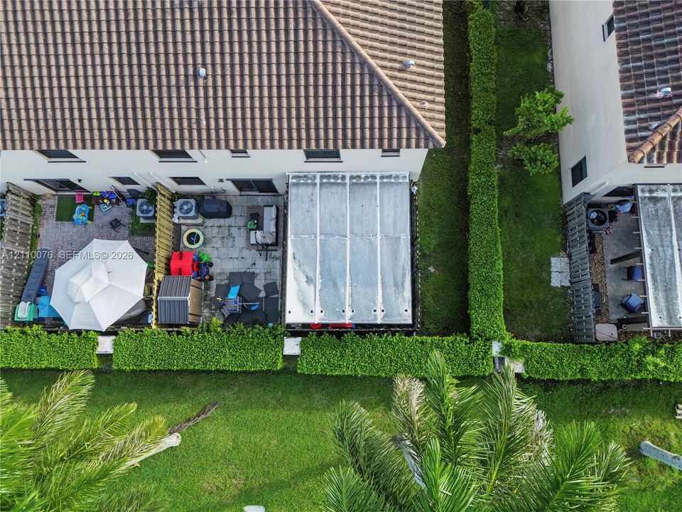Aerial view featuring a paved backyard patio with a metal-framed roof structure, concrete tile roofing, and perimeter hedging