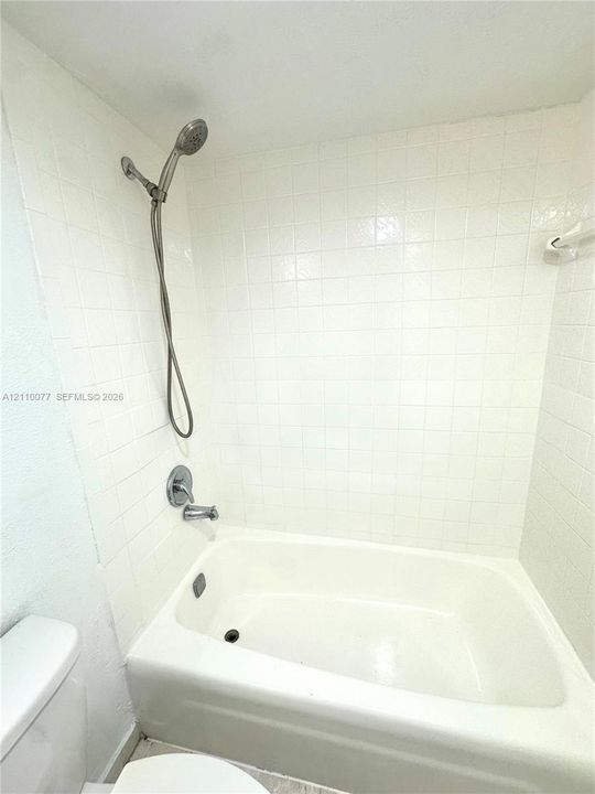 Full-height white square tile surround, tub-shower combination with a handheld shower fixture, and polished metal plumbing hardware