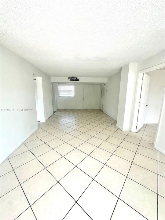Neutral interior space featuring large-format diagonal tile flooring, textured ceilings, and an exterior entry door with a rectangular window