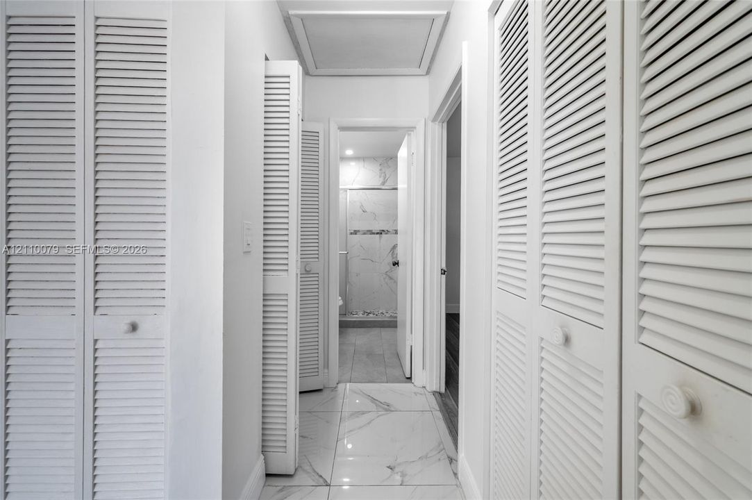 Hallway featuring large-format tile flooring with a neutral finish, multiple white louvered-style closet doors, and recessed ceiling lighting