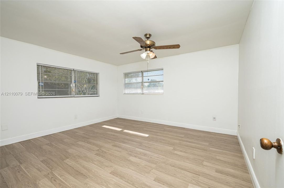 Interior space featuring wood-finish flooring, dual windows with horizontal blinds, and a central ceiling fan with an integrated light fixture