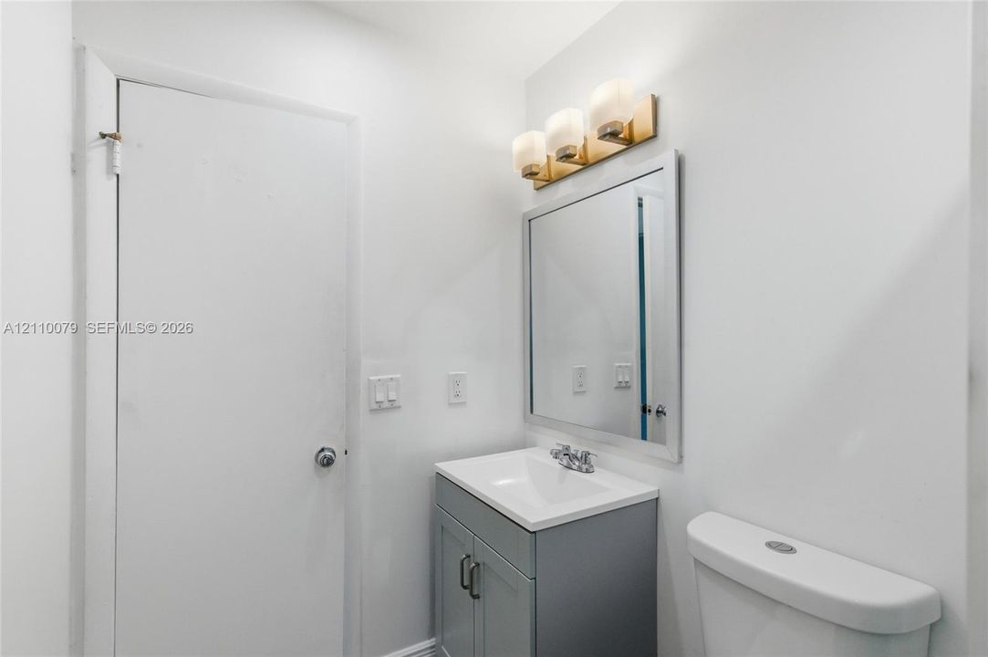 Gray vanity with a white countertop and basin, three-light fixture with glass shades, and a rectangular mirror with a metal frame