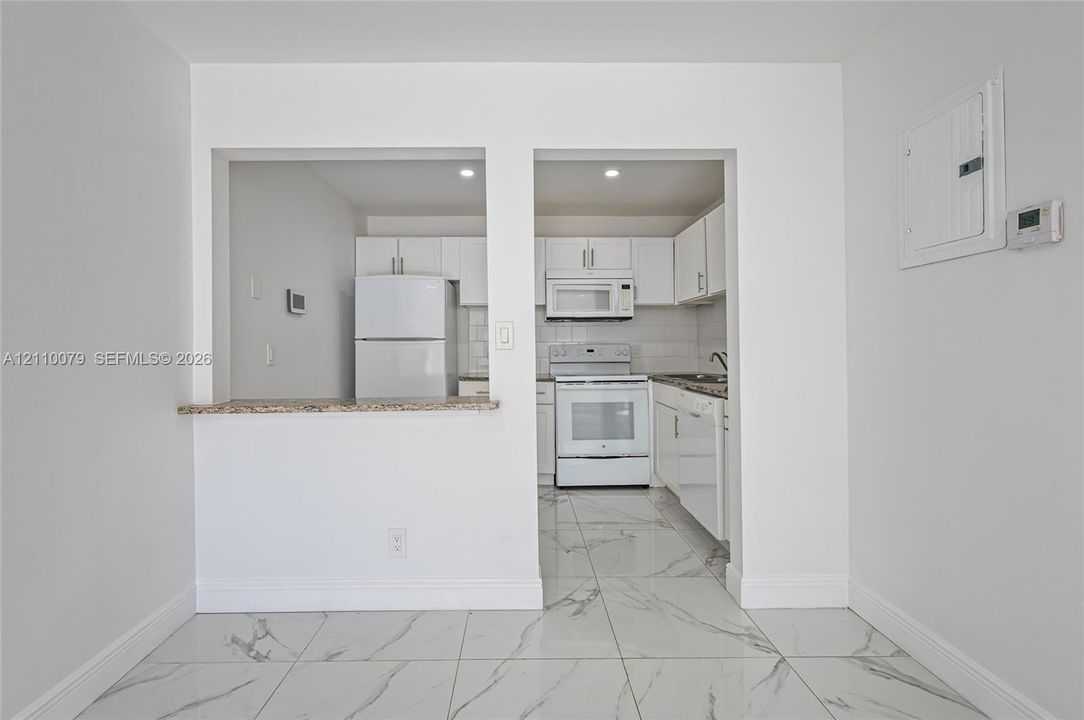Kitchen featuring white cabinetry, stone-finish countertops, tile flooring, and integrated white appliances