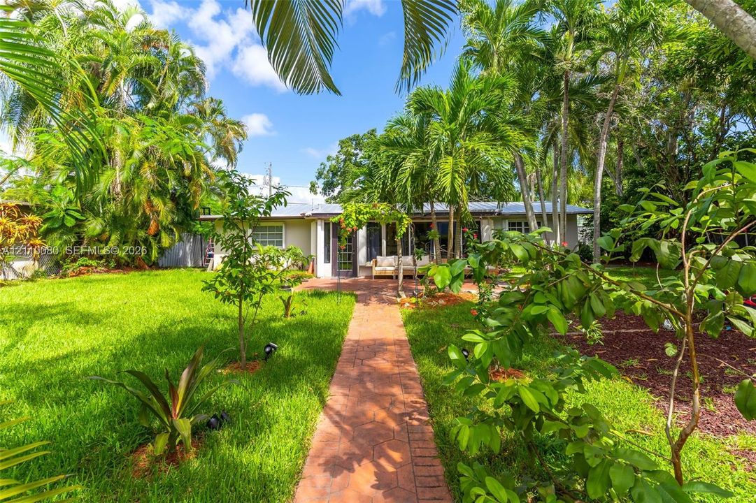 Expansive backyard featuring a patterned stone paver walkway, mature palm trees, established landscaping, and a ground-level concrete patio