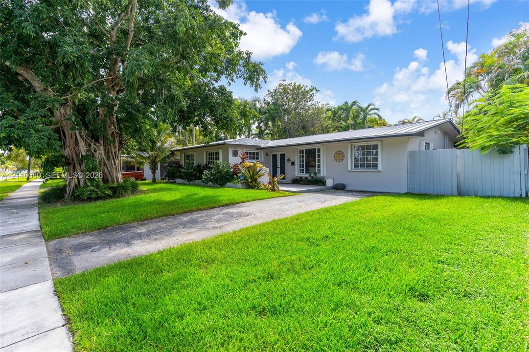 Single-story exterior featuring a metal roof, paneled siding, multi-pane windows, paved driveway, and mature landscaping