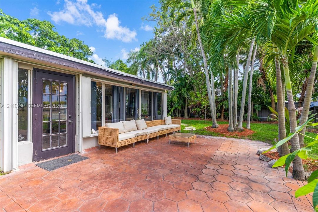 Exterior patio featuring hexagonal terracotta-toned pavers, mature palm trees, and floor-to-ceiling windows