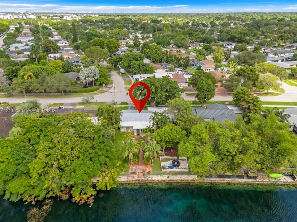 Waterfront property featuring a metal roof, brick paved walkway, stone seawall, and established tropical vegetation