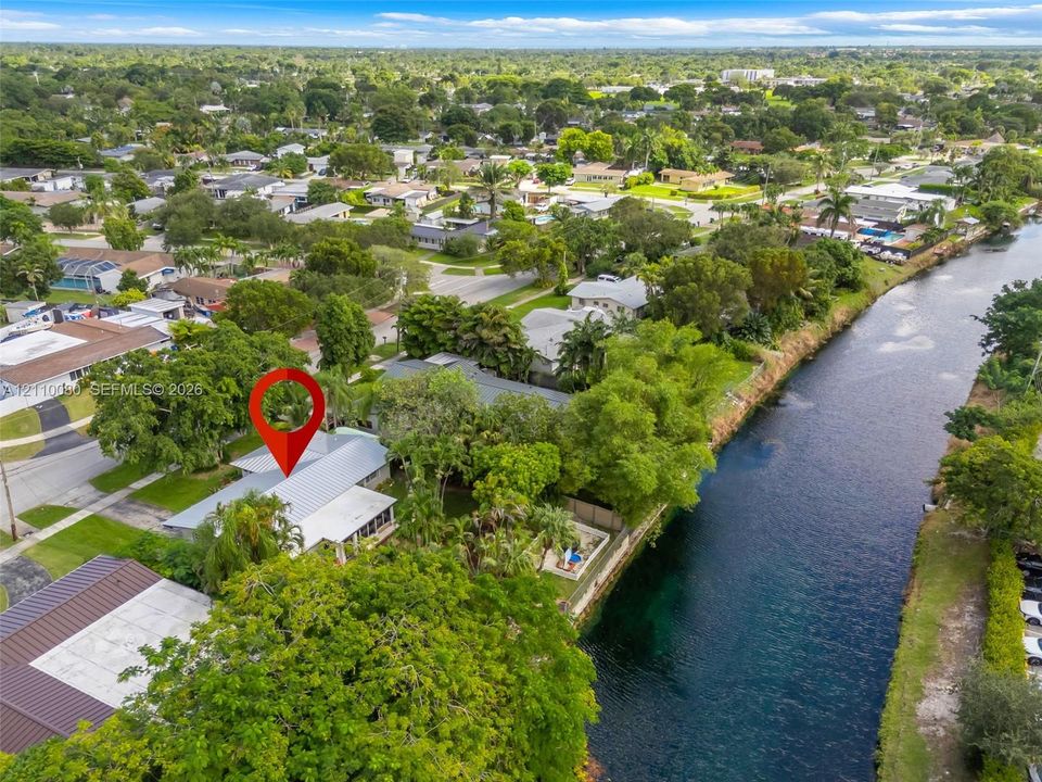 Aerial perspective of a waterfront property featuring direct canal frontage, a metal roof, screened-in porch, and mature landscaping