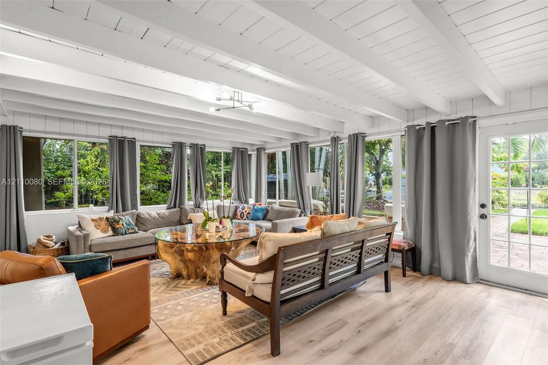 Sunroom featuring vaulted ceilings with exposed beams, wood-finish flooring, extensive floor-to-ceiling windows, and a glass-paned exterior door
