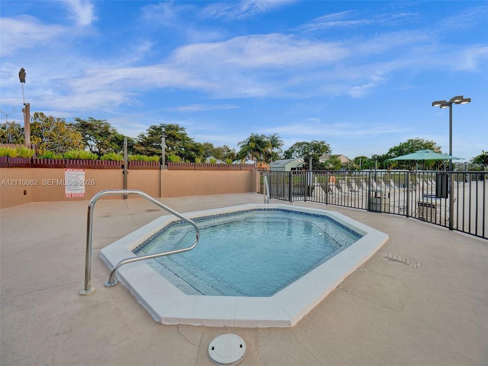 In-ground spa with tile detailing, concrete deck, and metal perimeter fencing
