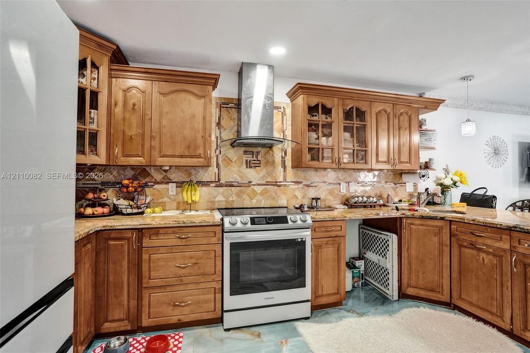 Kitchen featuring natural wood cabinetry with glass-panel upper doors, stone-surface countertops, decorative tile backsplash, stainless steel range, and a wall-mounted stainless steel chimney-style range hood