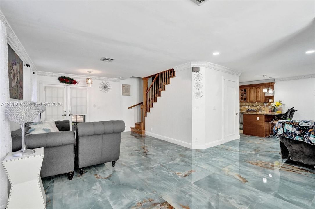 Large-format polished stone flooring with distinct veining, crown molding, wooden staircase with slatted balustrades, and recessed ceiling lighting