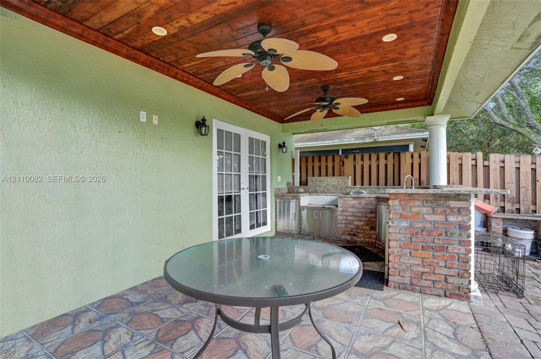 Covered patio featuring a stained wood plank ceiling, dual ceiling fans, recessed lighting, and stone tile flooring