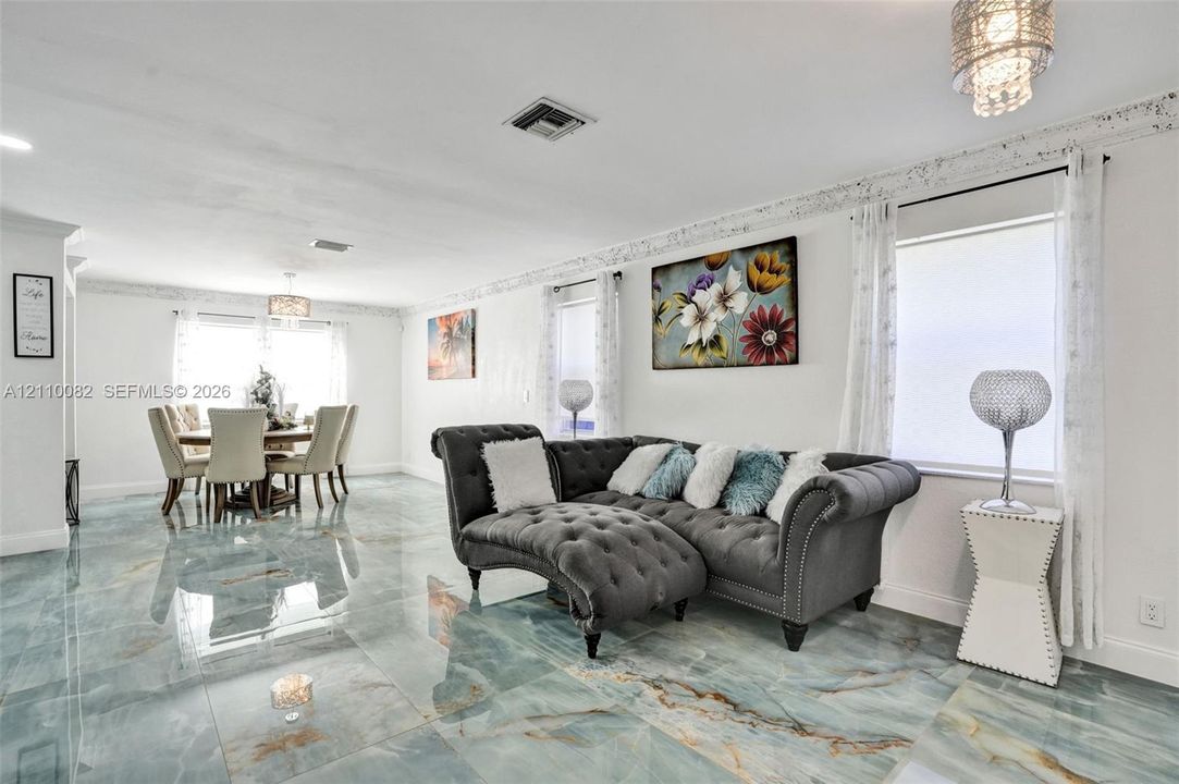 Open-concept area featuring polished stone-finish floor tiling, intricate crown molding, and tiered crystal-style pendant lighting