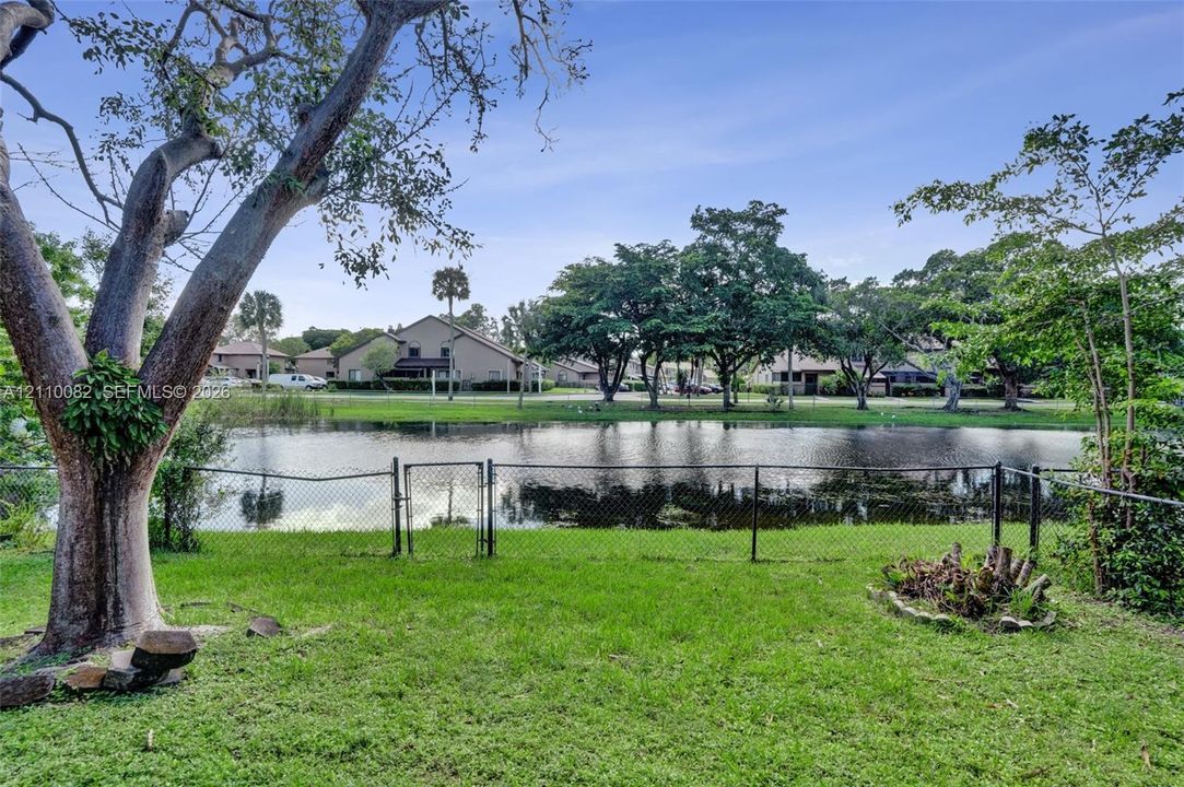 Backyard featuring a grass lawn, chain-link perimeter fencing, mature trees, and a water frontage
