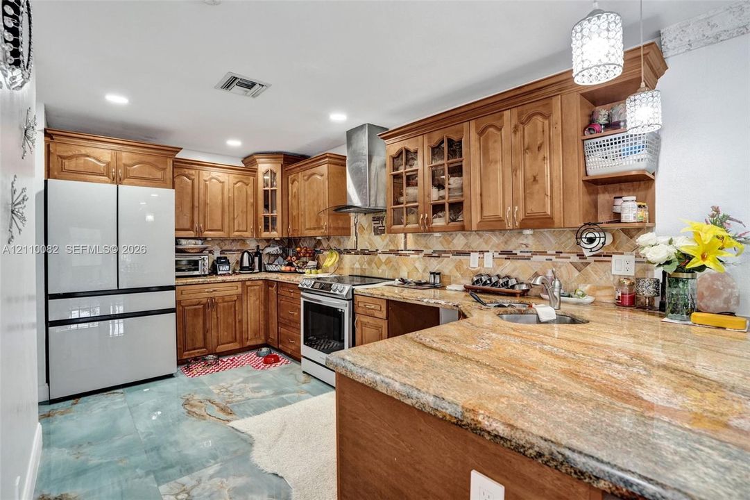 Kitchen featuring wooden cabinetry, stone-surface countertops, stone tile backsplash, stainless steel range hood, and tile flooring