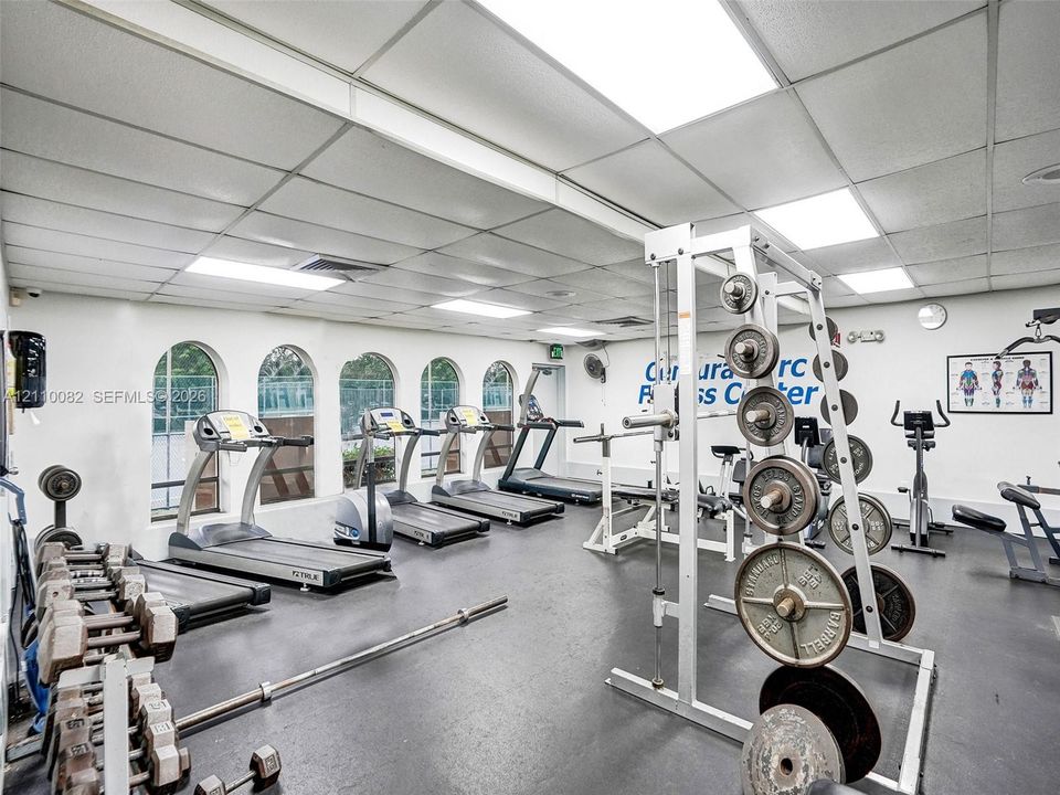 Fitness center featuring recessed lighting, a grid ceiling system, durable rubberized flooring, and multiple arched windows