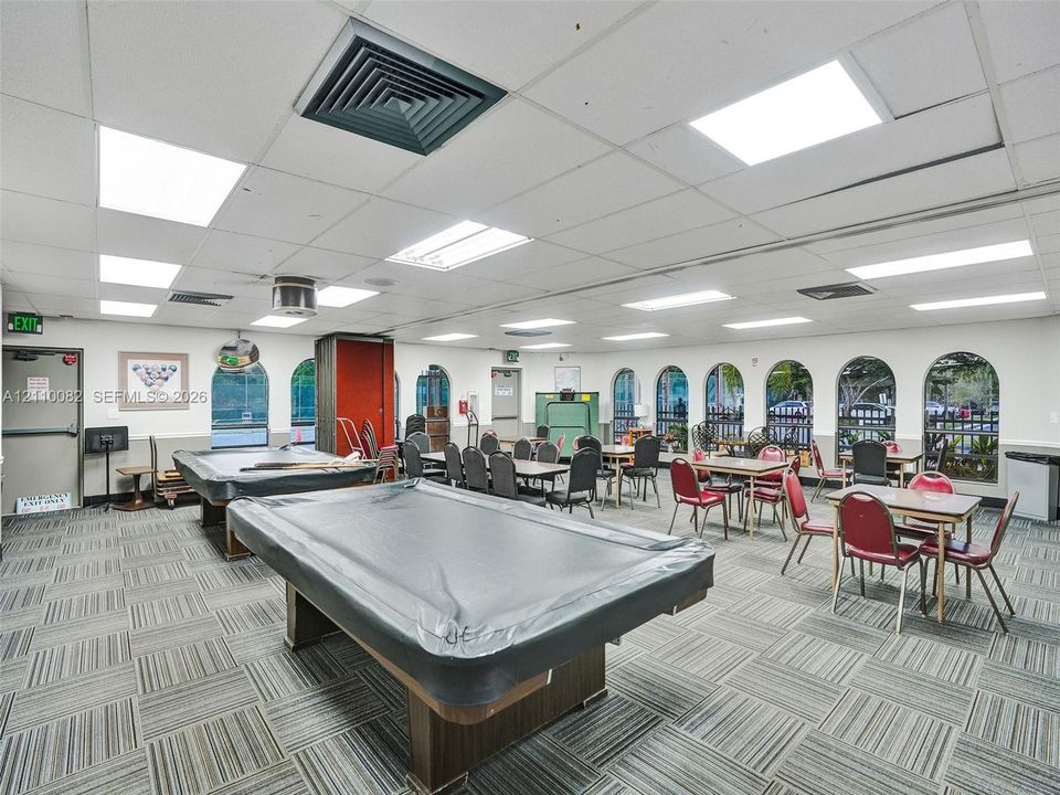 Large multipurpose room featuring a drop ceiling with integrated rectangular lighting, carpet tile flooring, and multiple arched windows