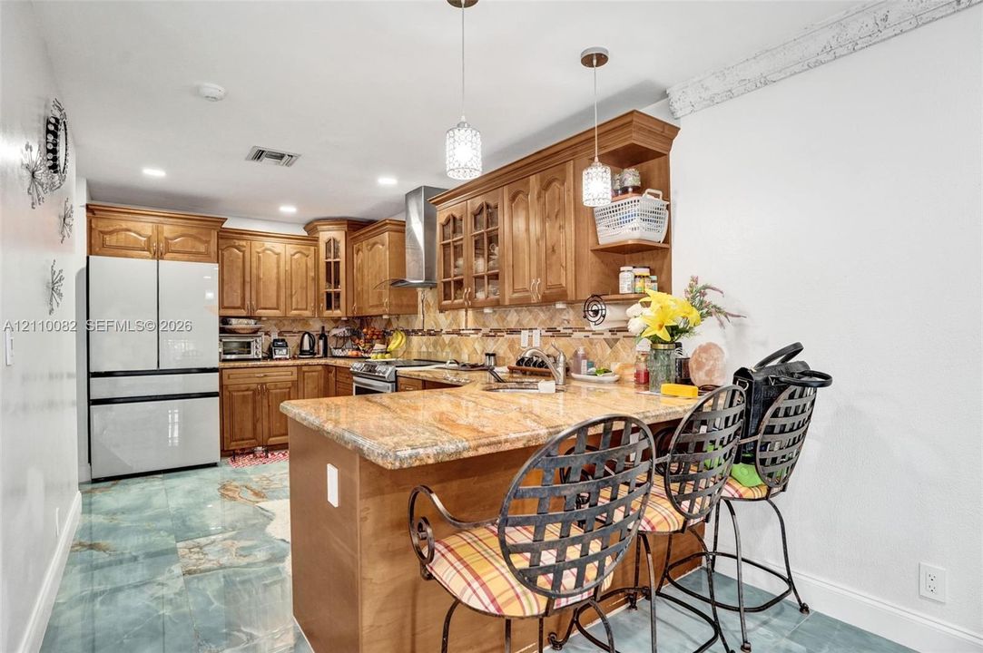 Kitchen featuring wooden cabinetry, stone-surface countertops, tile backsplash, stainless steel range hood, and pendant lighting