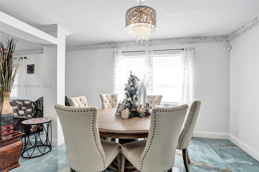 Dining area featuring large-format tile flooring, decorative crown molding, and a suspended multi-tiered crystal chandelier