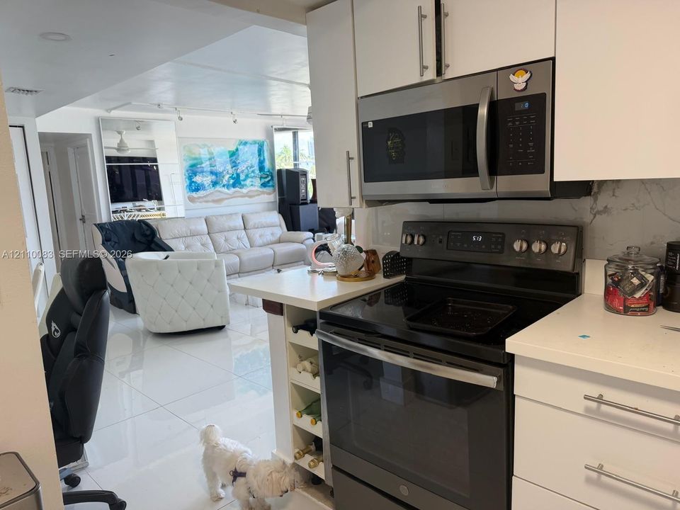 Kitchen featuring white cabinetry, light-toned stone-finish countertops, stainless steel microwave, black electric range, and integrated wine storage shelving