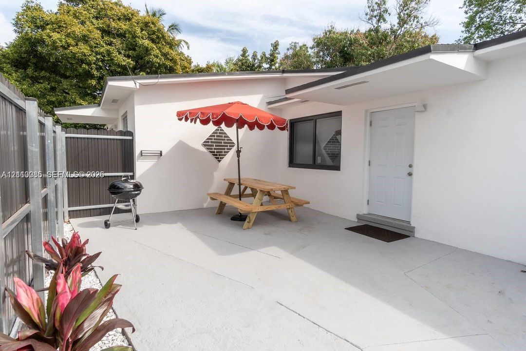 Concrete patio featuring a vertical wood-slat privacy fence, exterior white stucco siding, and dark-trimmed window frames