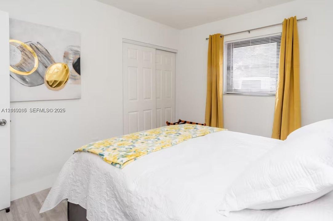 Bedroom featuring light-toned wood-finish flooring, a double-panel sliding closet door, and a horizontal window with adjustable metal blinds
