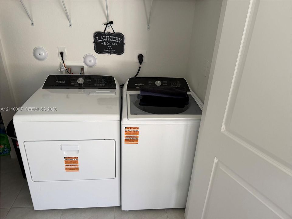 Utility area featuring side-by-side white clothes washer and dryer units, integrated utility hookups, and overhead wall-mounted shelving