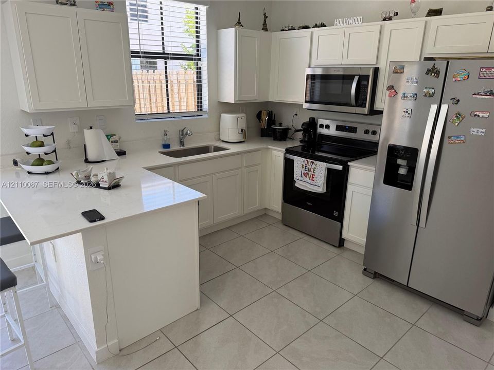 Kitchen featuring white shaker-style cabinetry, white countertops with an integrated breakfast bar, stainless steel appliances, and tile flooring