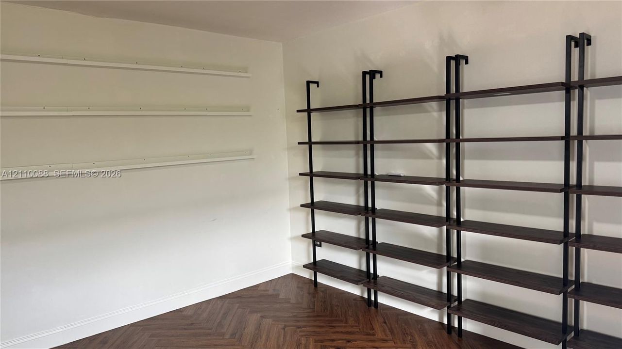 Herringbone wood-finish flooring featuring floor-to-ceiling dark wood-finish shelving with black metal supports, complemented by wall-mounted horizontal shelving