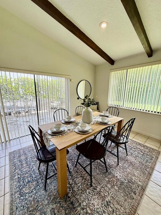 Vaulted ceiling with exposed wood-finish beams, tile flooring, and sliding glass patio door