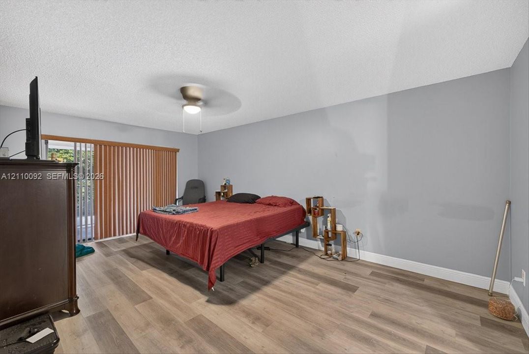 Room featuring wood-finish flooring, a ceiling fan with integrated lighting, and vertical blinds covering the sliding glass door