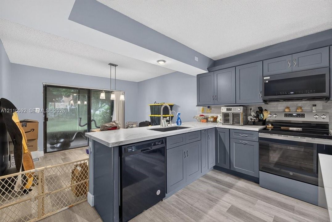 Kitchen featuring charcoal-toned cabinetry, light-toned countertop, undermount sink, stainless steel appliance suite, and wood-finish flooring