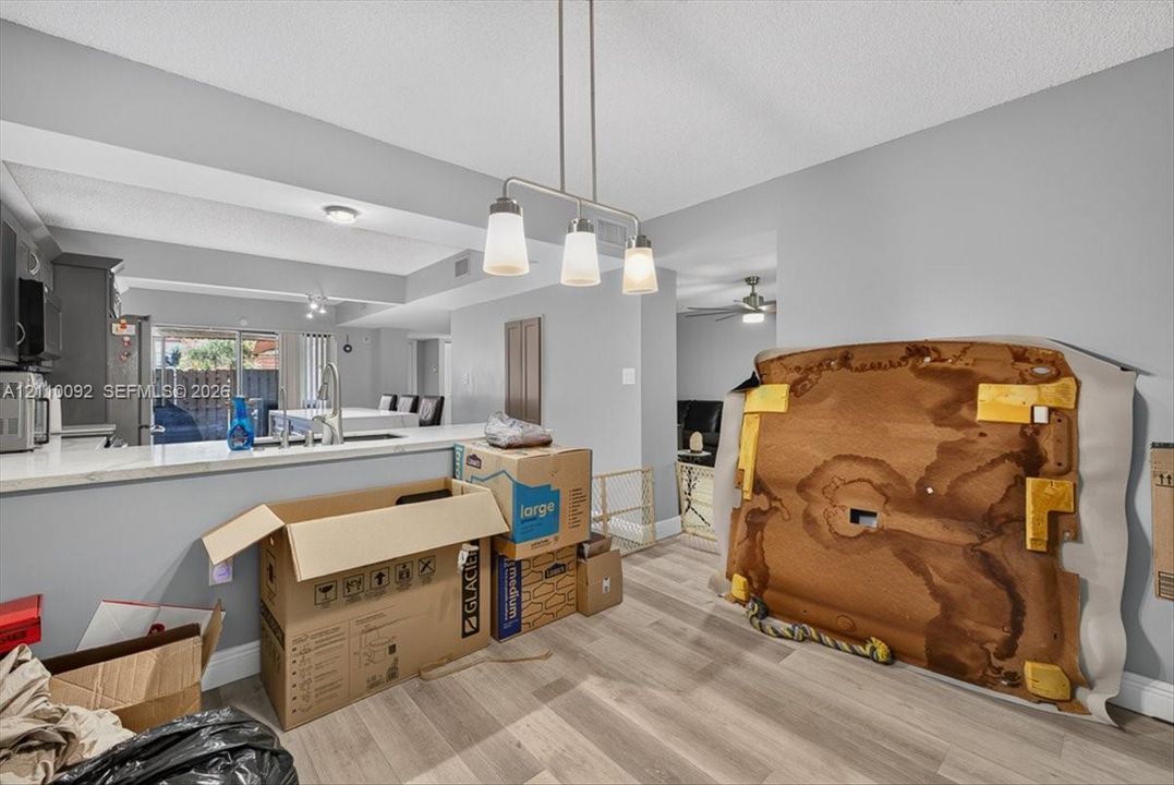 Kitchen featuring a pass-through counter, stone-finish countertops, stainless steel undermount sink, three-light linear pendant fixture, and wood-finish flooring