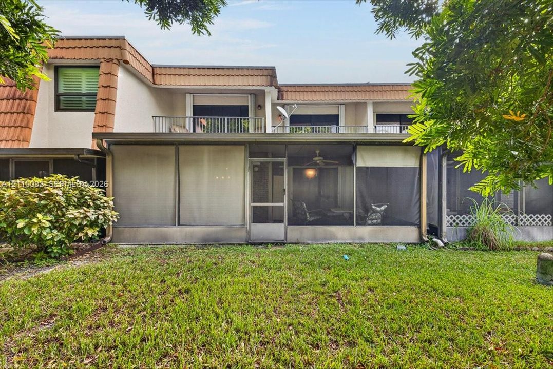 Multi-level exterior featuring a screened-in ground floor patio, upper-level balcony with metal railing, stucco siding, and clay-tile roof detailing